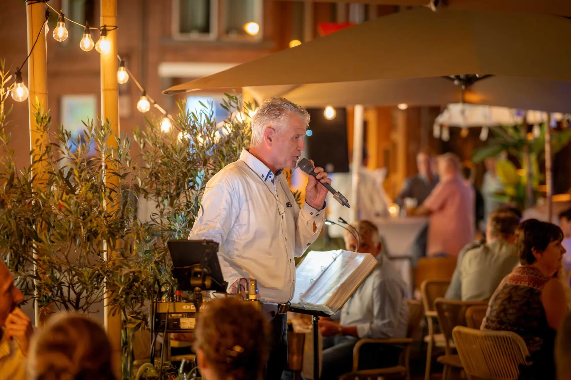 Een zanger met microfoon op het terras van Blend in de avond, onder de lichtsnoeren
