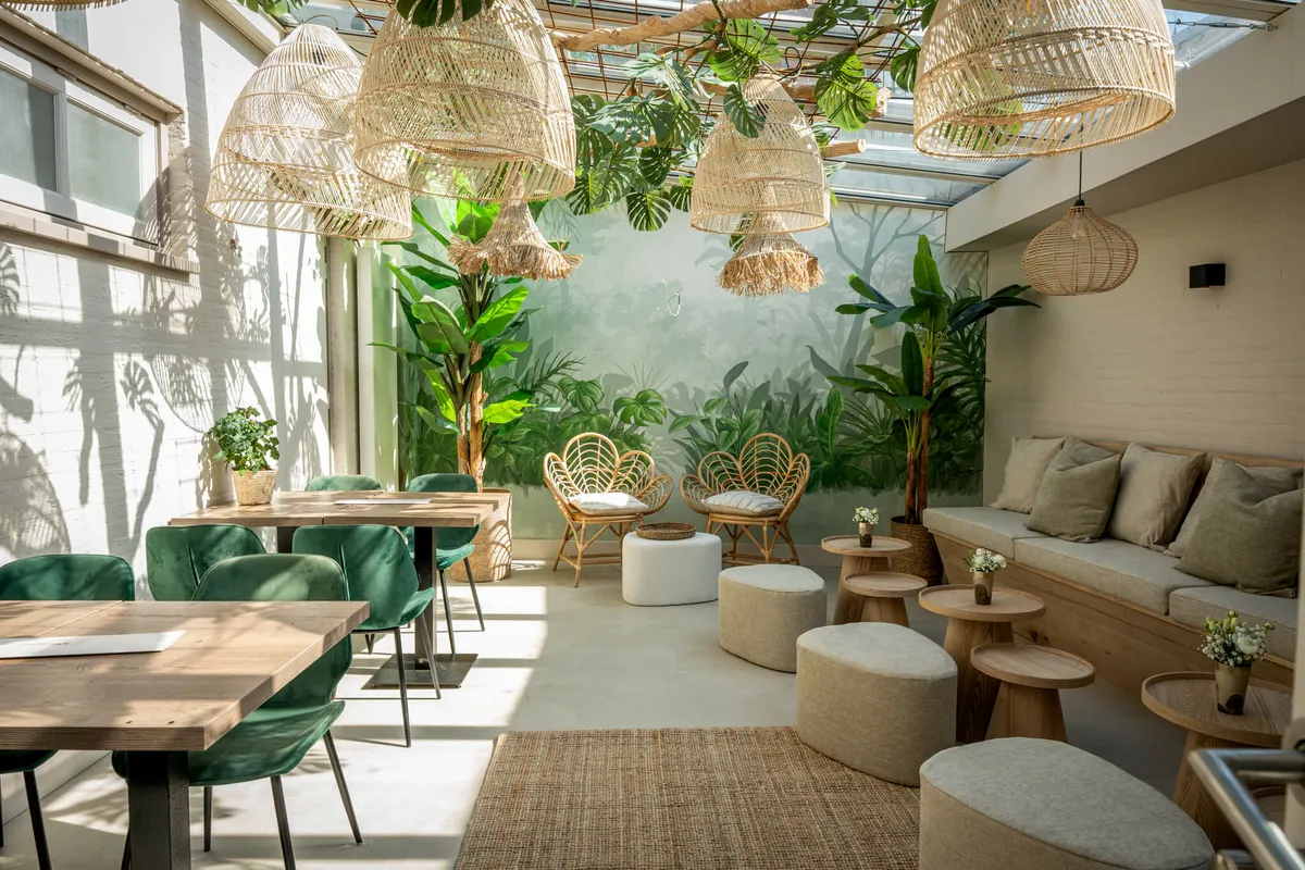 De lounge van Blend met rotan lampen, planten en groene fluwelen stoelen