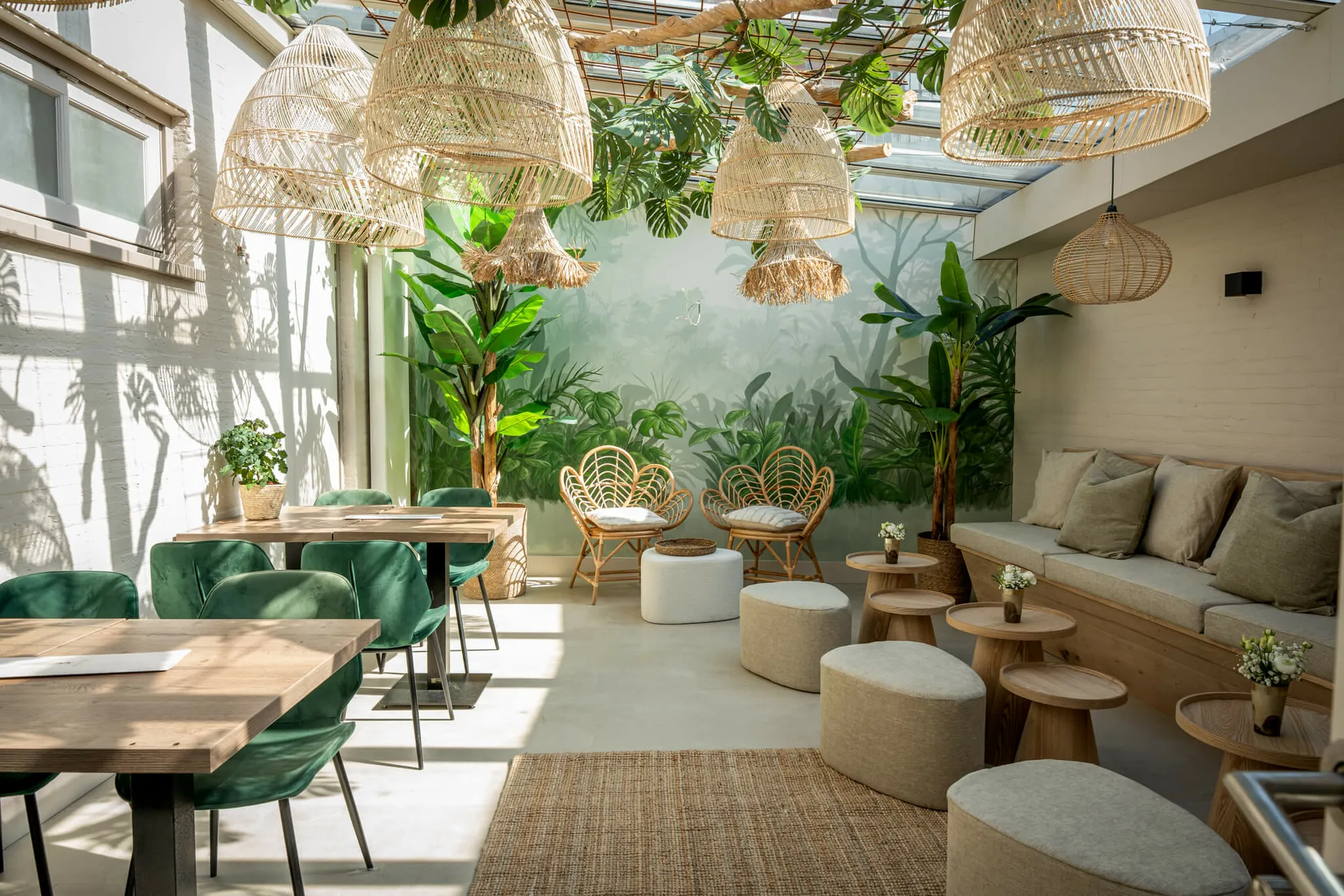 De lounge van Blend: rotan lampen, een jungle-muurschildering en groene fluwelen stoelen in het daglicht