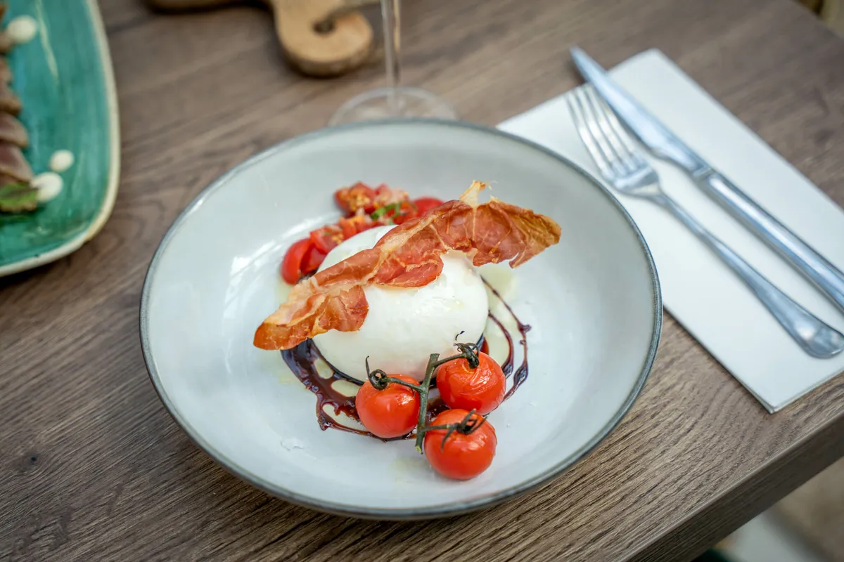 Burrata met tomaat en krokante ham op een bord bij Blend
