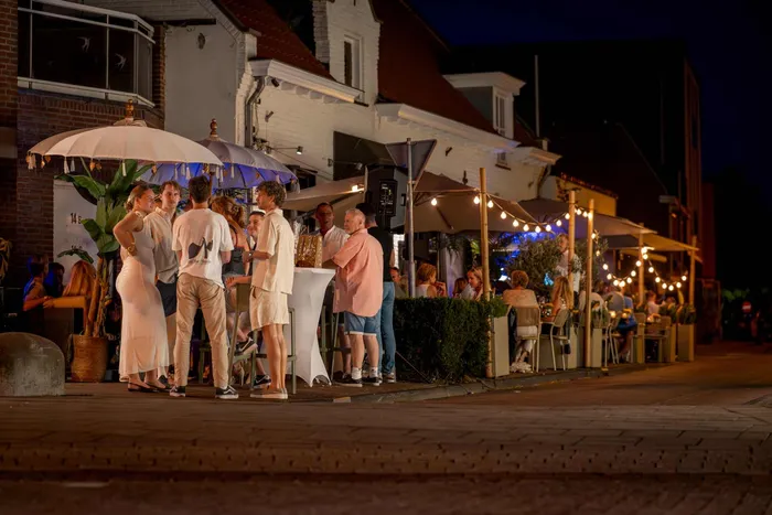 Gasten op het terras en op straat, in de avond onder de lampjes
