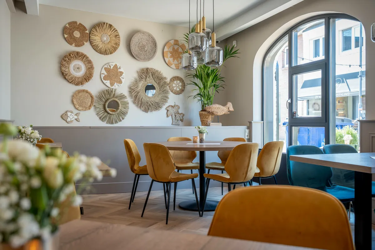 Ronde tafel met oker fluwelen stoelen onder een wand vol rieten manden, naast het boogvenster