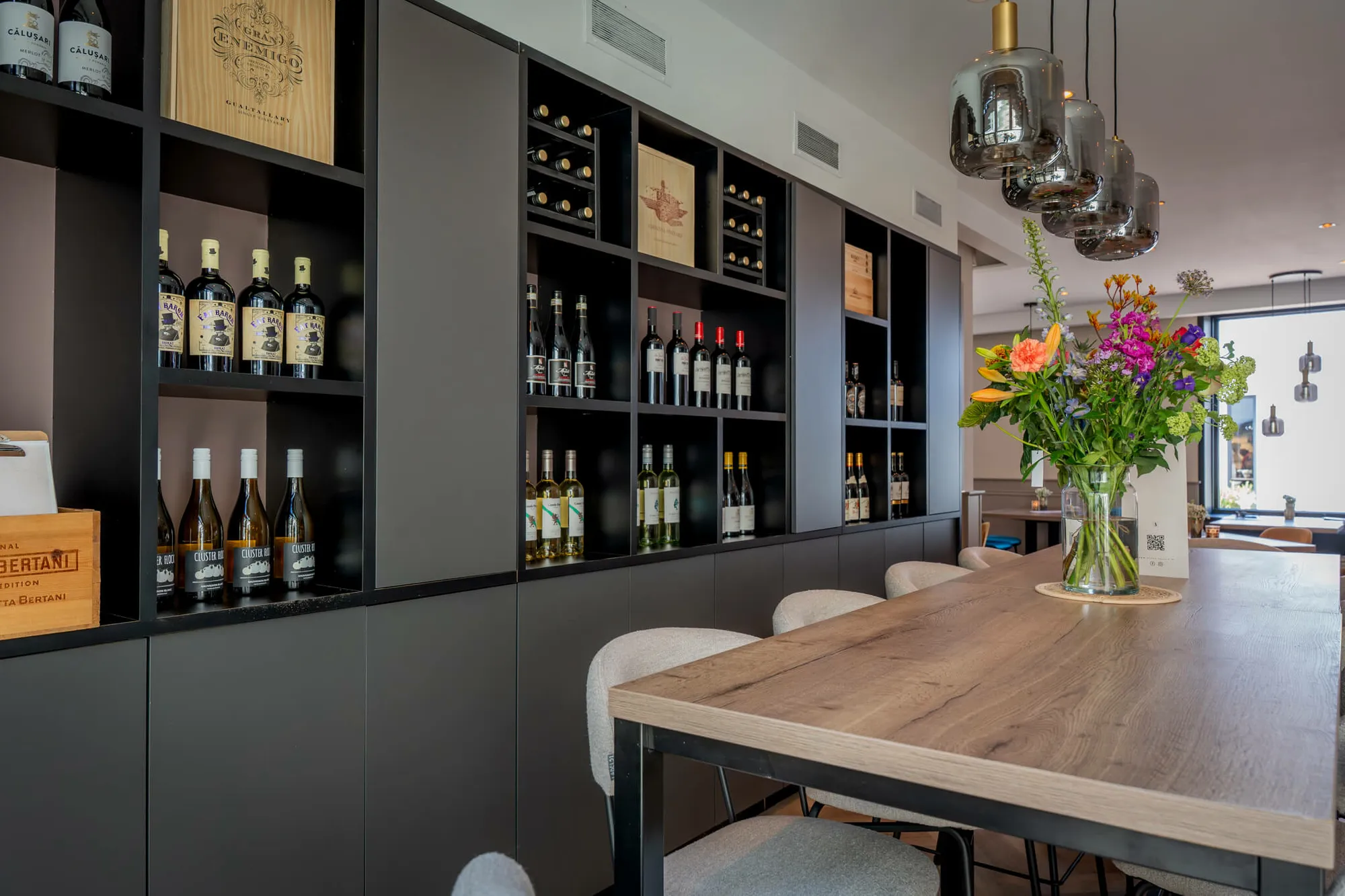 De wijnkast achter de bar van Blend met verse bloemen op de tafel